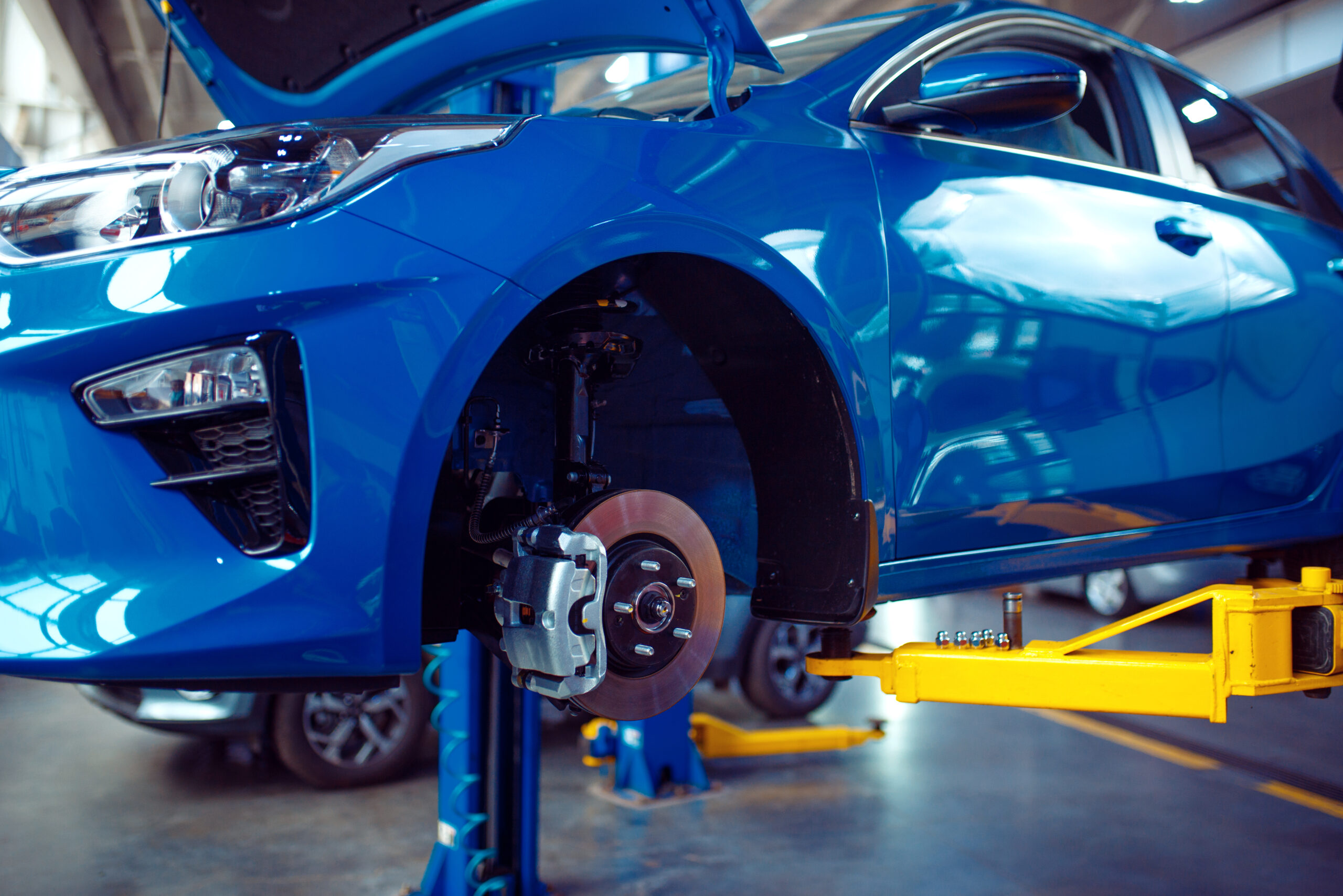 Vehicle with removed wheel on lift, car service station, nobody. Automobile garage interior, checking, diagnostics and repair equipment